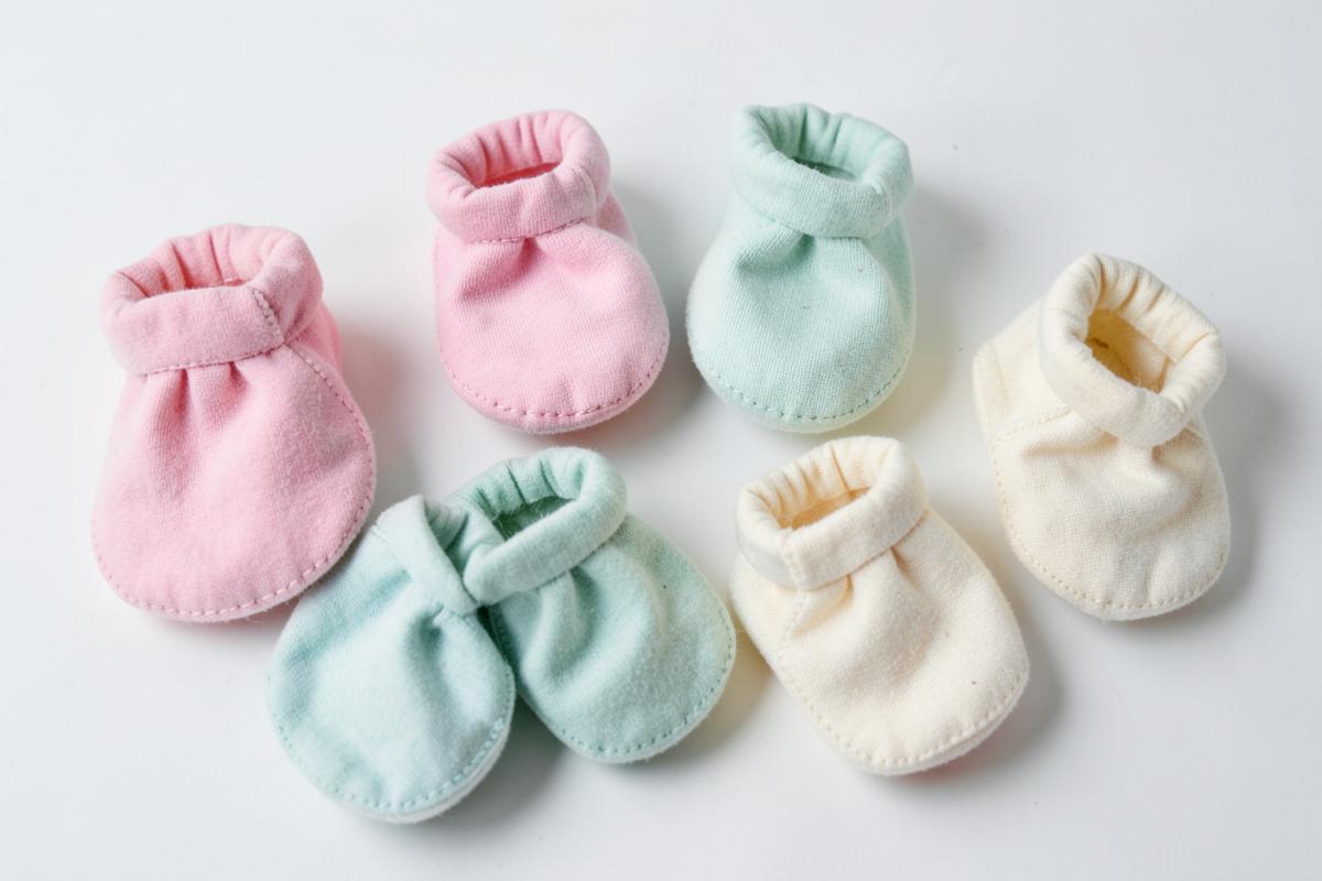 Vários sapatinhos de bebê feitos à mão em tons pastel dispostos sobre fundo claro